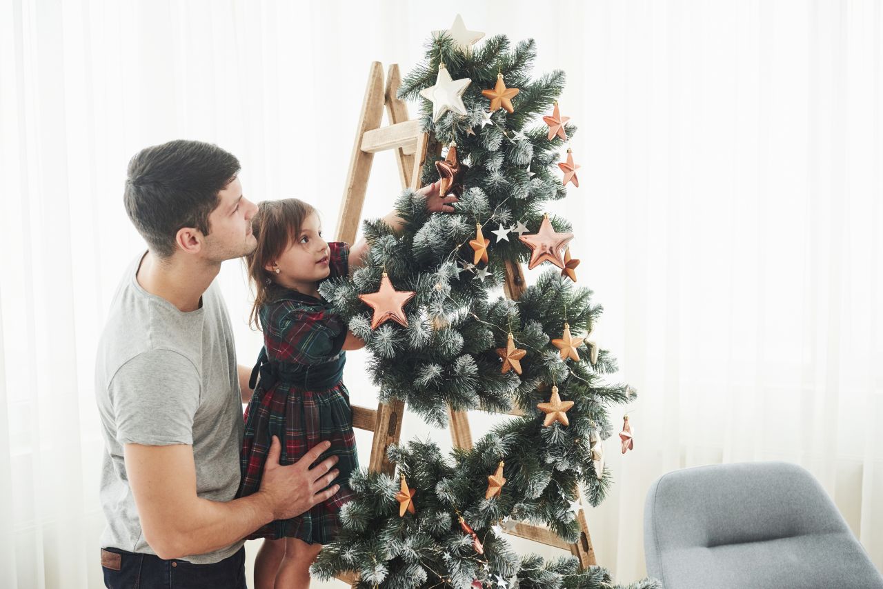 Girl decorating beautiful Christmas tree with stars while her father holds her.